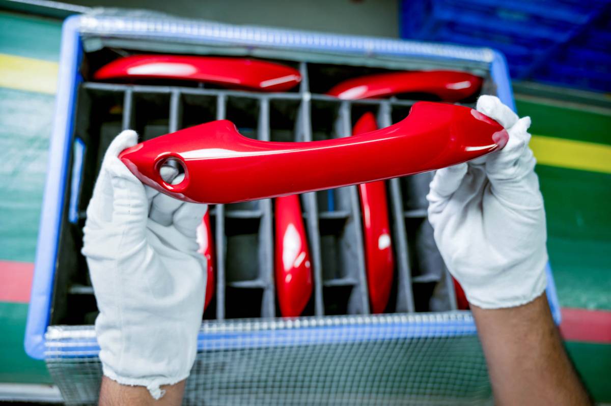 Two hands holding a red car door handle painted by Huf India.