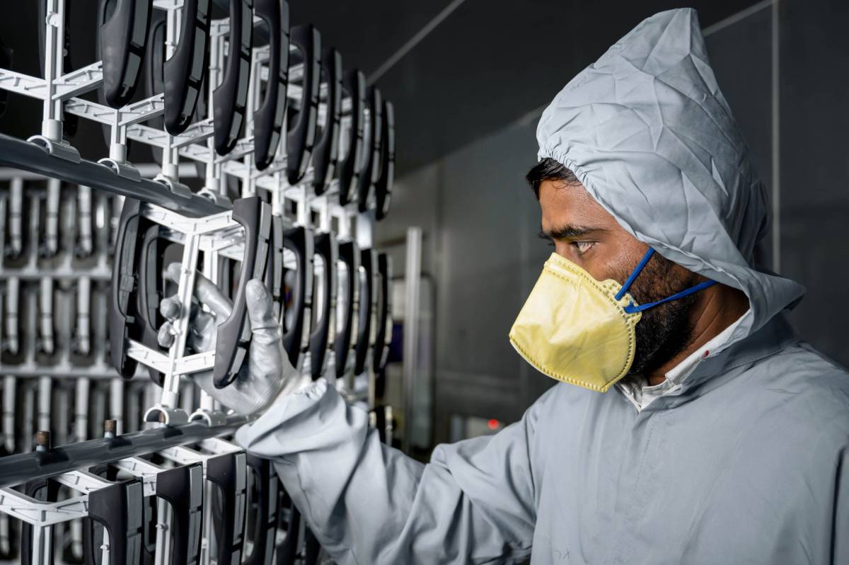 Employee of Huf India wearing a mask holds a painting rack in the paint shop.