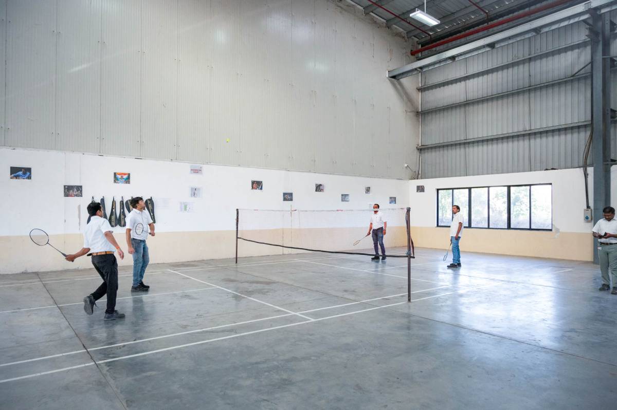 Huf India employees playing badminton in a gym.