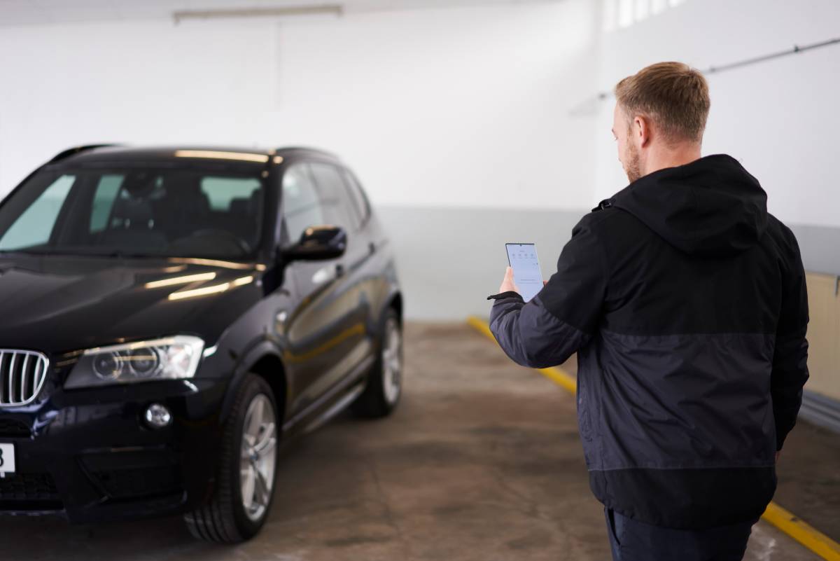 Man holding a smartphone in front of a BMW SUV.