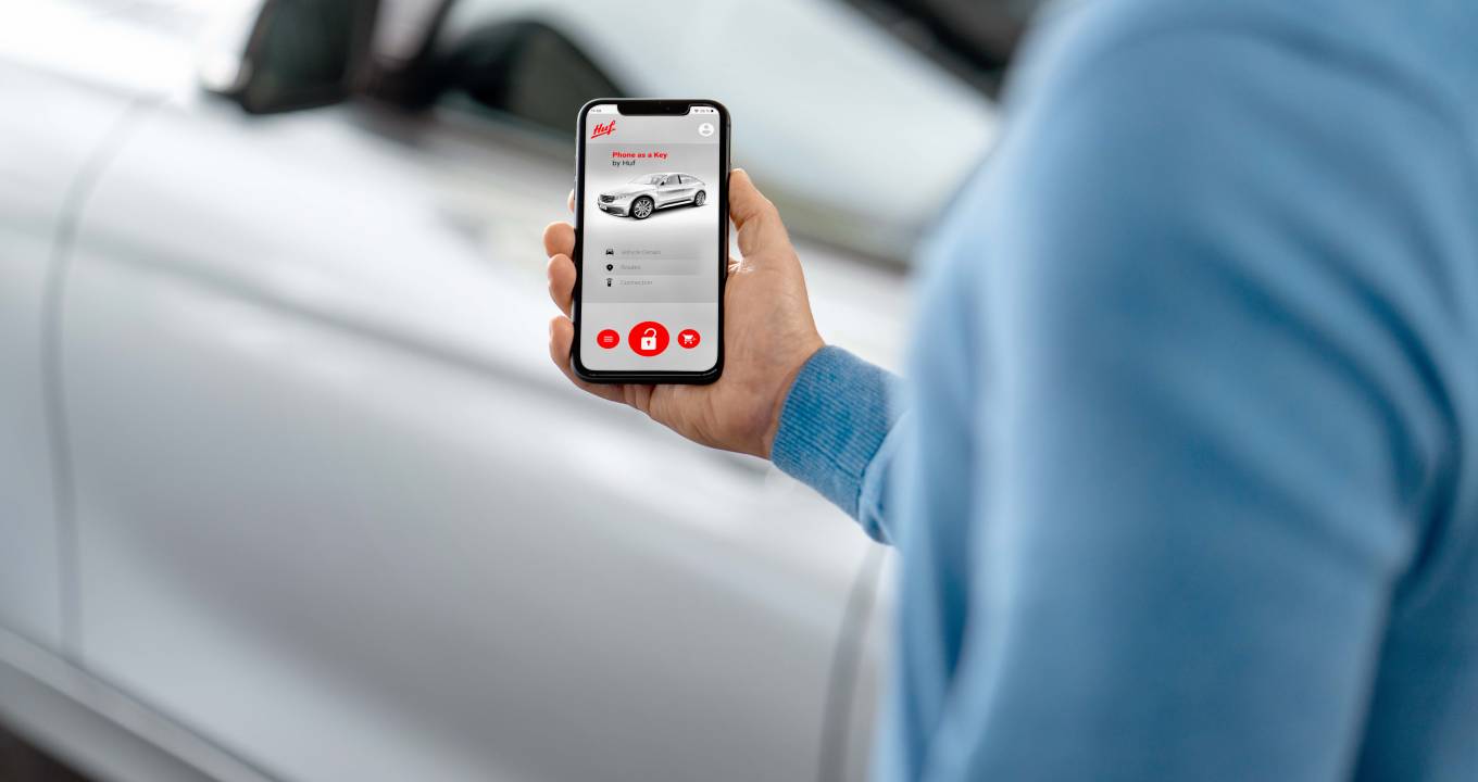 Person holding a smartphone with Phone as a Key app from Huf, gaining keyless handsfree access to a car.